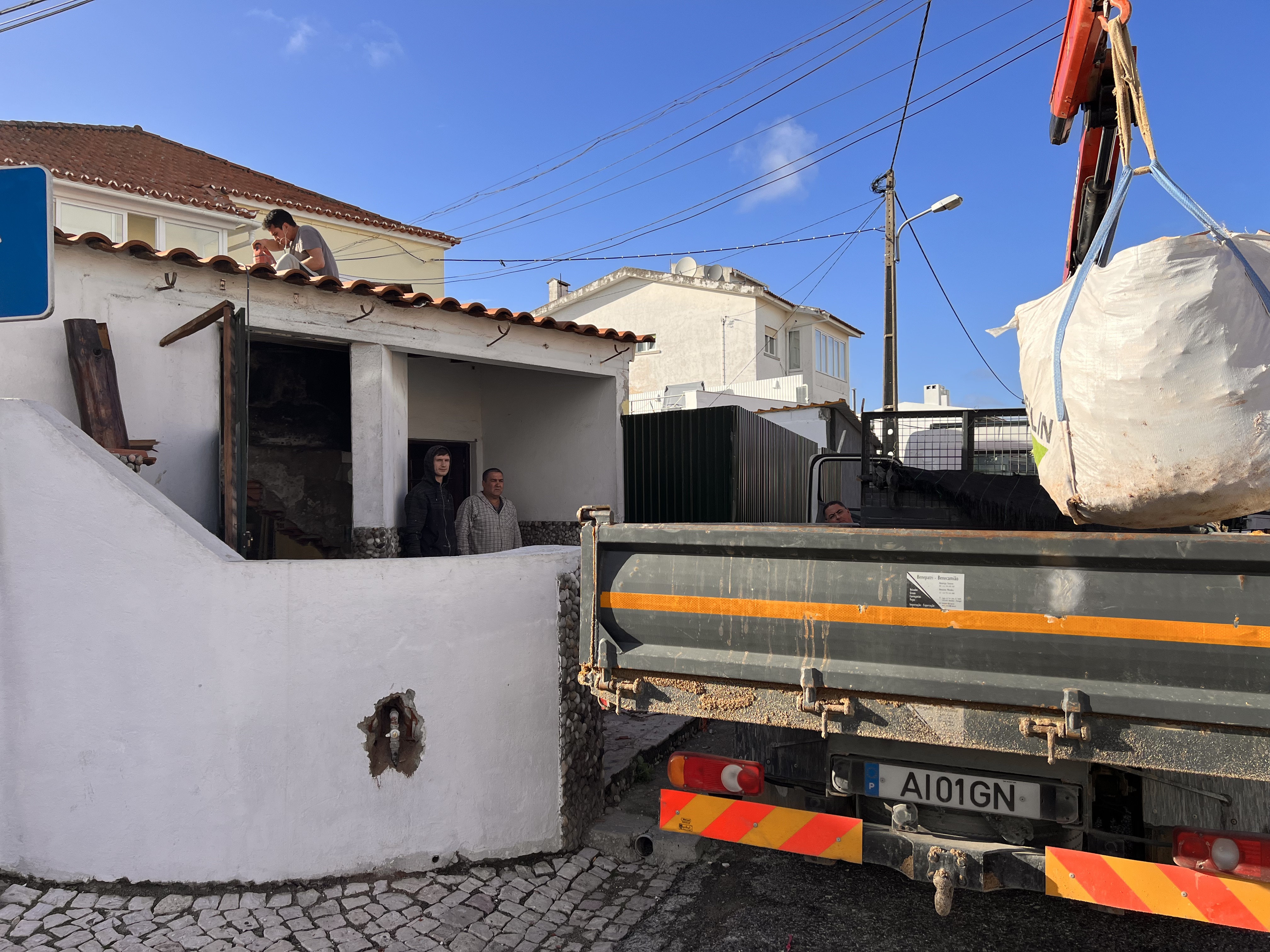 The Tasca during &mdash; skip bag of demolition waste lifted by crane from the tavern facade, a worker repairing the tile coping above the door