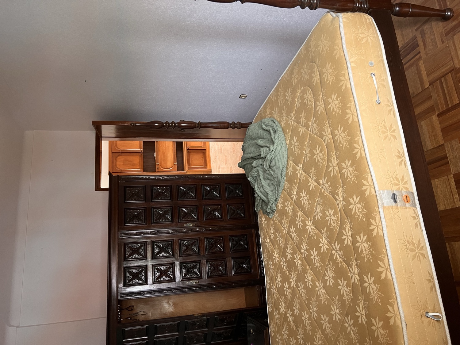 Vista before &mdash; original bedroom with a heavy dark-wood carved headboard, single mattress, parquet floor