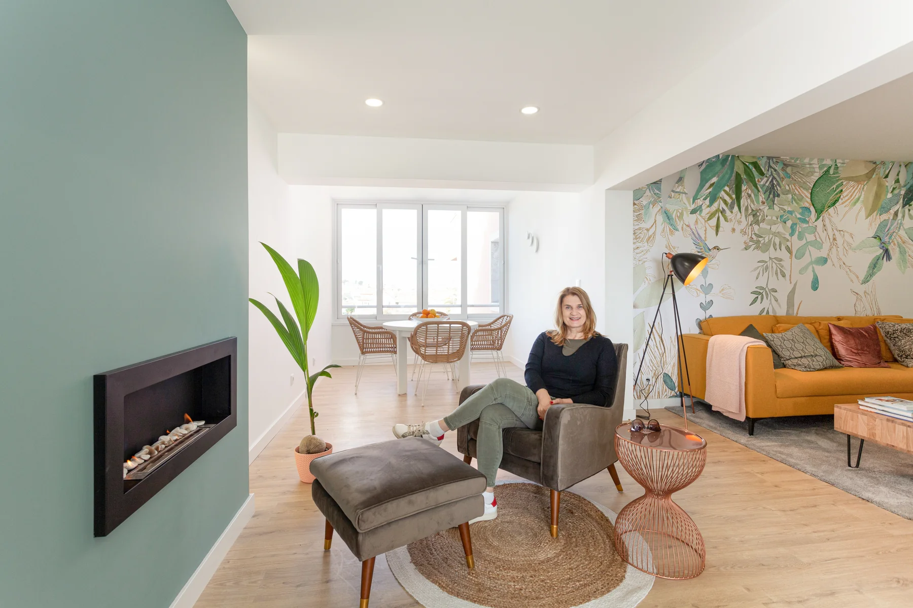 Maja Milič in a finished living room — teal fireplace wall, pale oak floors, botanical wallpaper