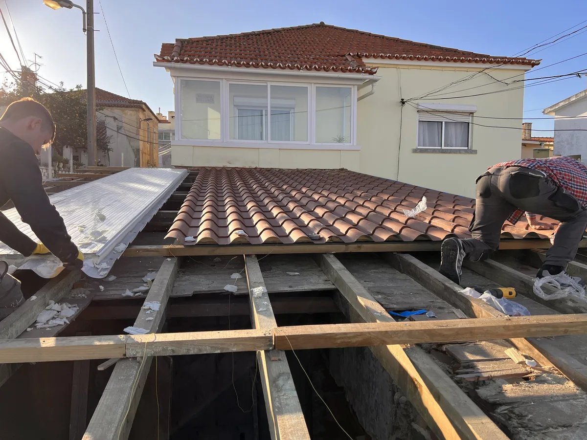 The Tasca em obra &mdash; dois trabalhadores a assentar o novo telhado em telha terracota, metade da inclinação já telhada, a outra metade ainda em barrotes abertos com isolamento por baixo