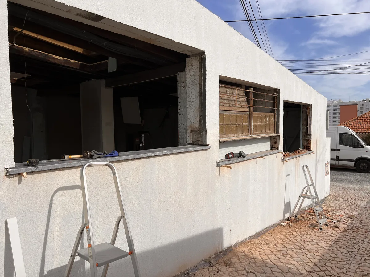 The Tasca em obra &mdash; aberturas de janela rasgadas na parede lateral, escadotes e ferramentas à espera na rua de calçada lá fora