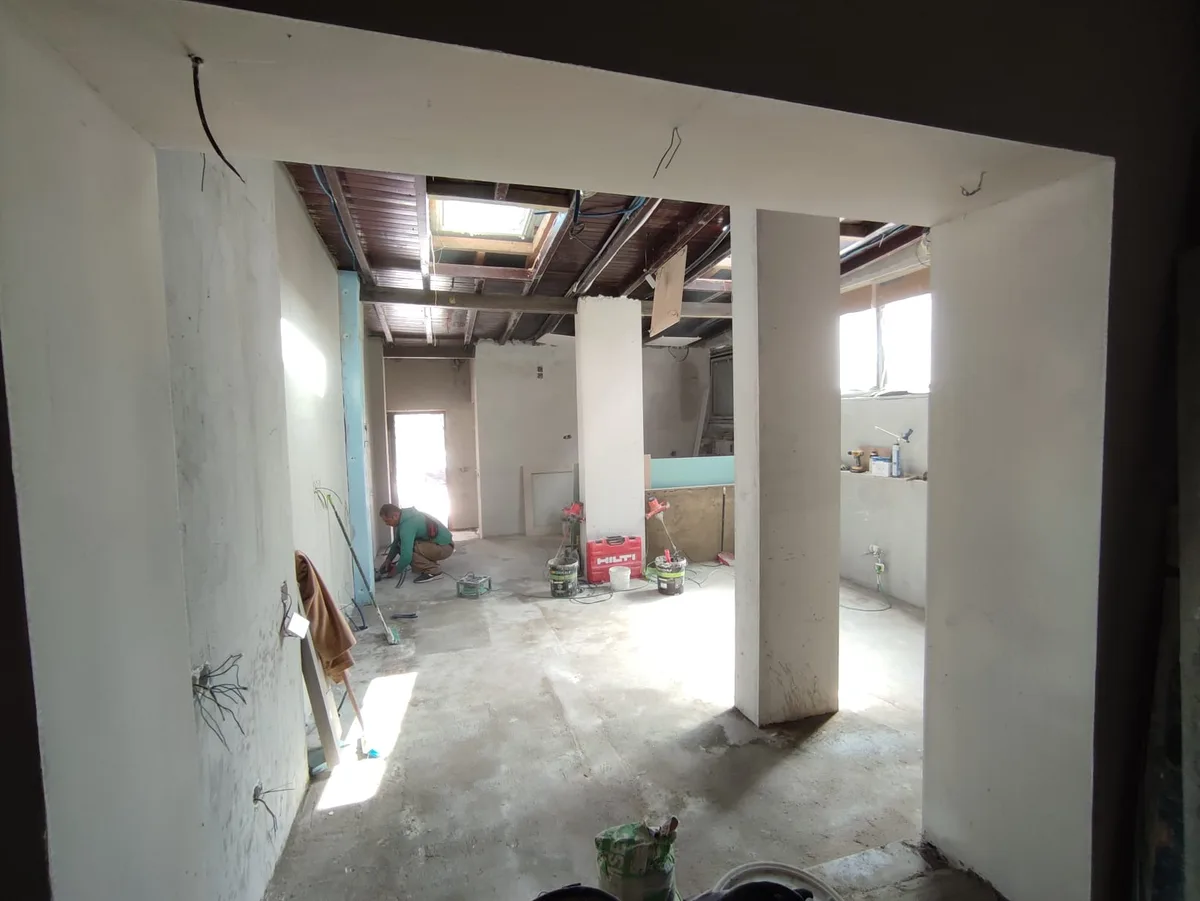 The Tasca em obra &mdash; sala open-plan a ganhar forma, paredes estruturais rebocadas, clarabóia rasgada no tecto de madeira, um trabalhador no chão a fazer os últimos retoques
