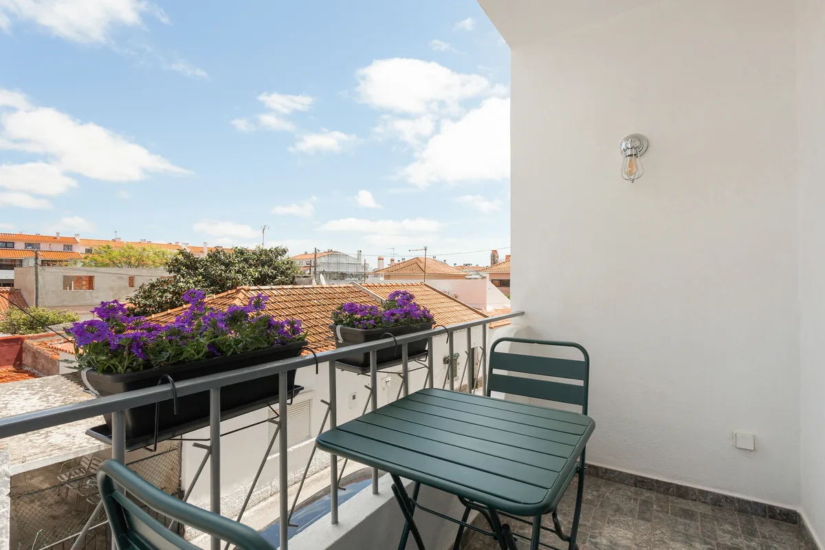 Figueiras — Varanda com uma pequena mesa e plantas floridas.