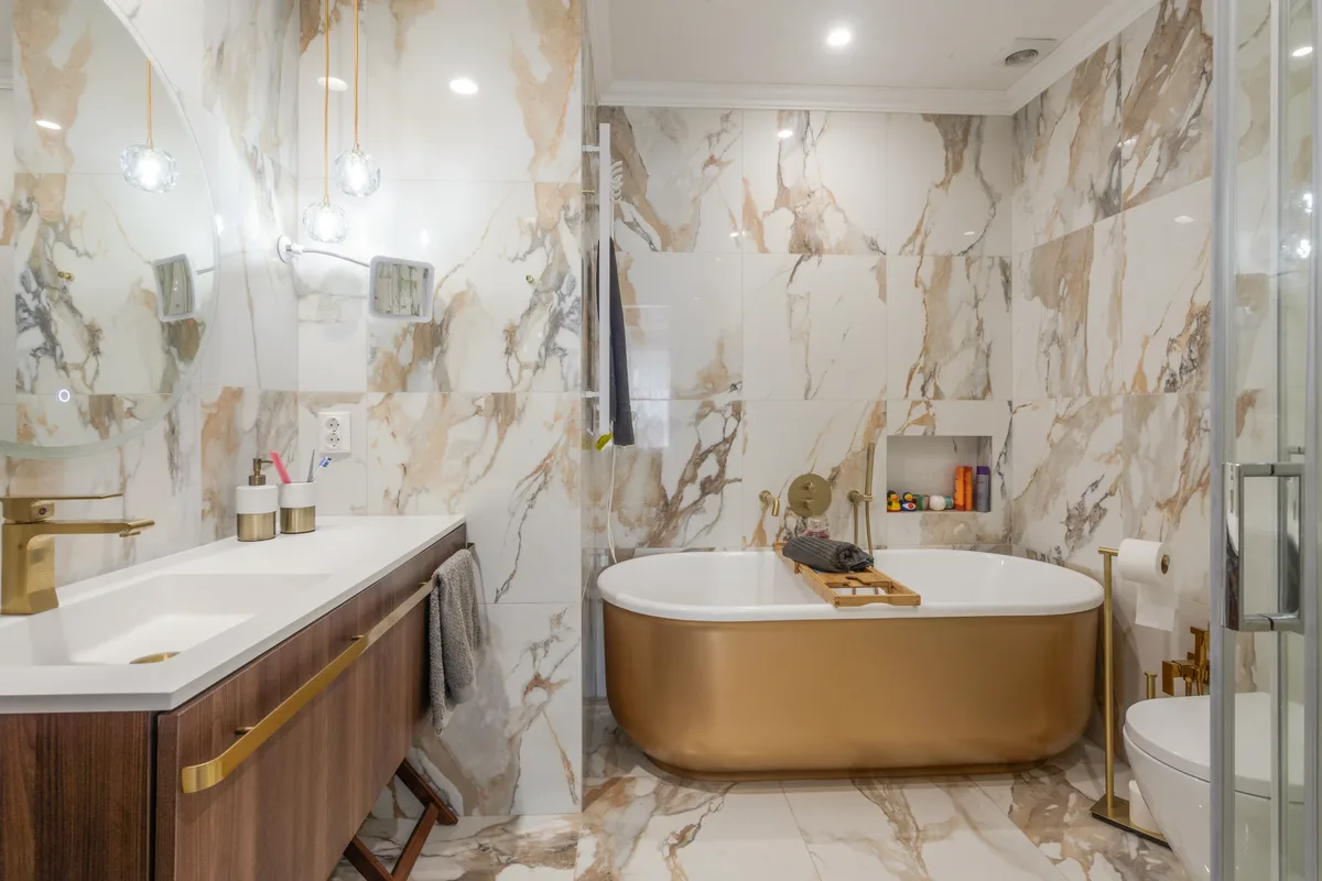 Rosa — Marble-patterned bathroom with a gold-coloured freestanding bath.