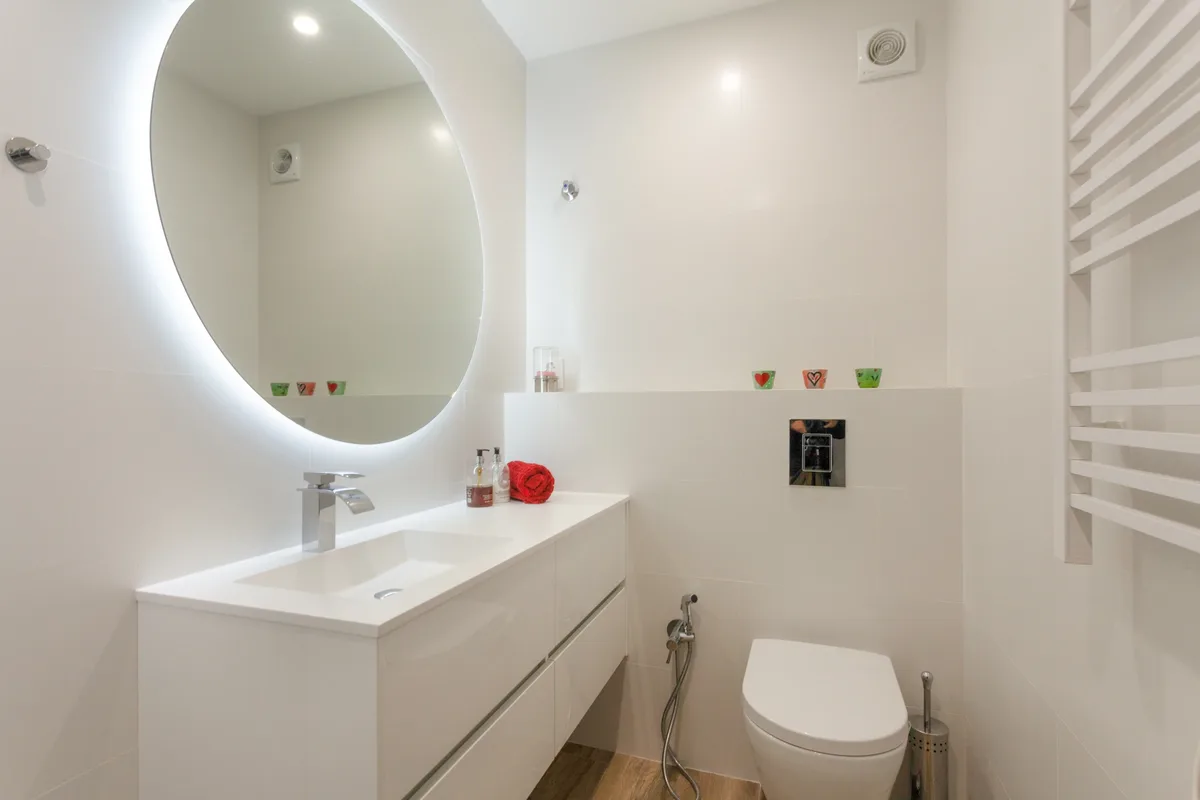 Rosa — White bathroom with an illuminated oval mirror.