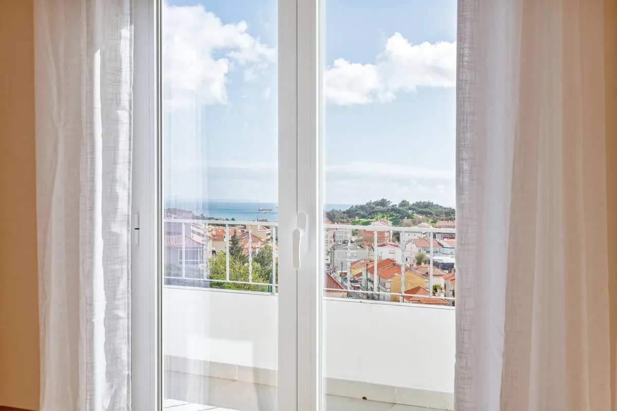 Vista — Balcony doors framing rooftops and the distant sea.