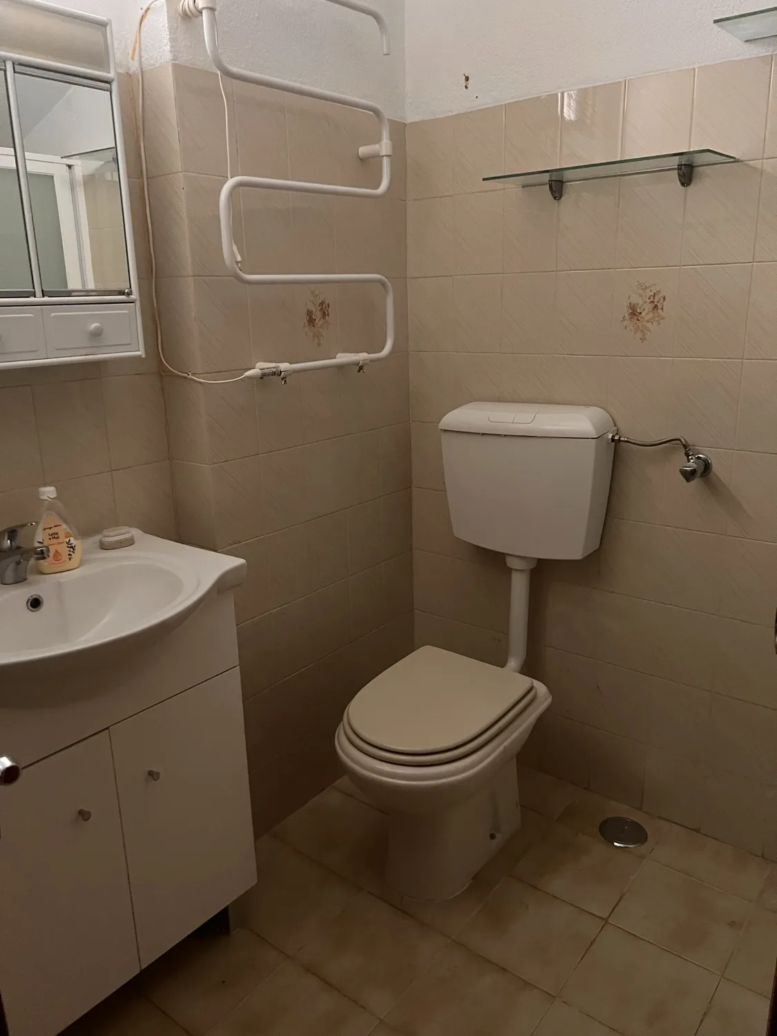 Vista before &mdash; cream-tiled bathroom with white toilet, wall-mounted sink, glass shower screen, and a towel-rail radiator