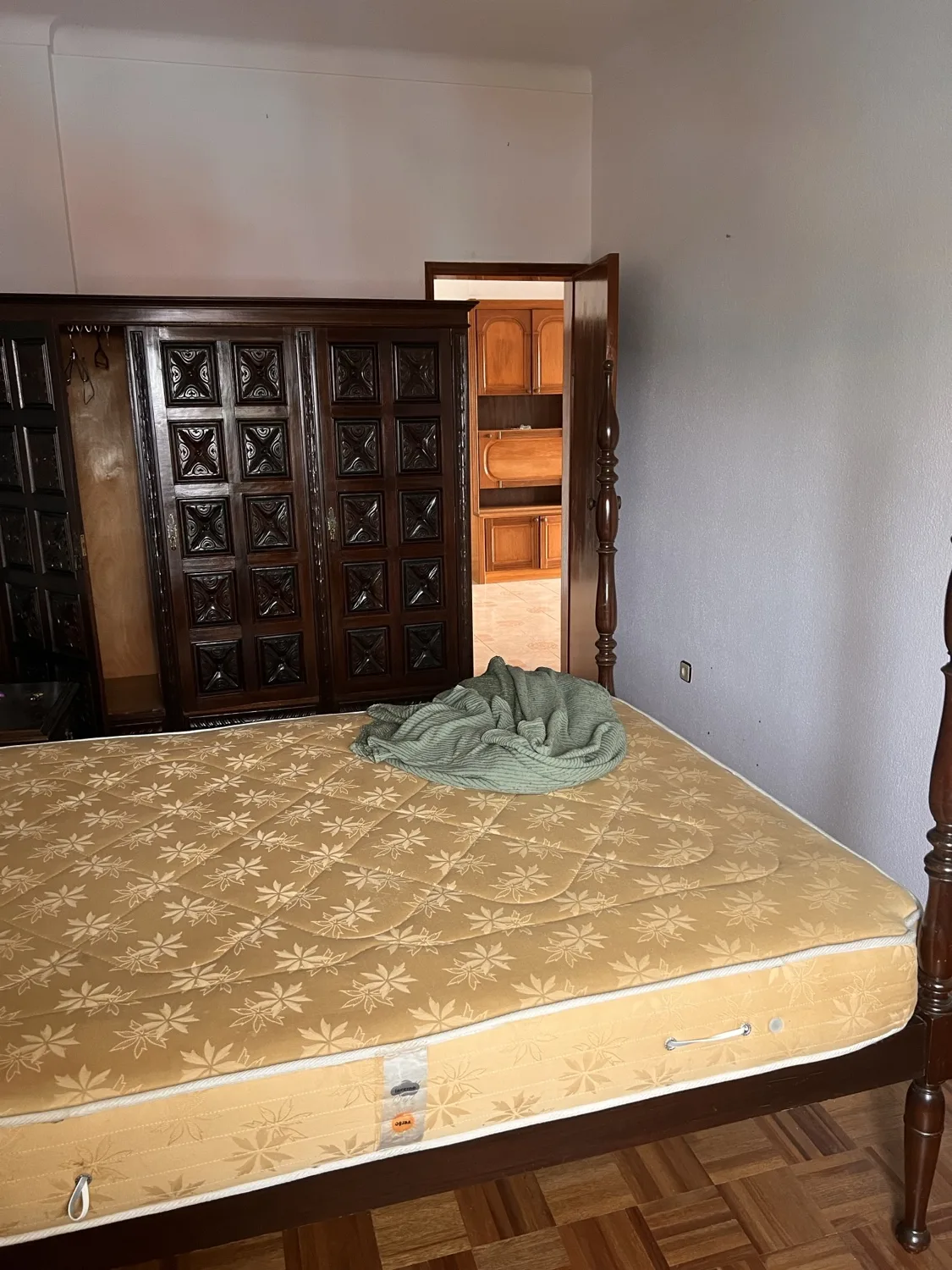 Vista before &mdash; original bedroom with a heavy dark-wood carved headboard, single mattress, parquet floor